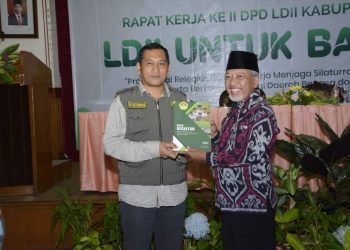 Ketua DPD LDII Gresik H. Abdul Muis Zuhri menyerahkan laporan kegiatan DPD LDII Gresik 2022 pada Kepala Badan Kesatuan Bangsa dan Politik Nanang Setiawan. Dok: LINES.