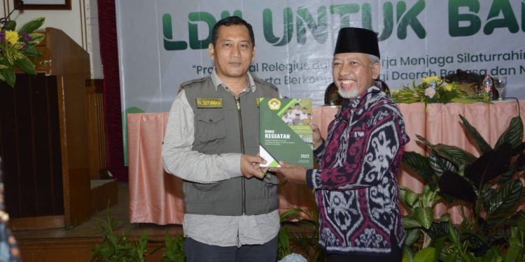 Ketua DPD LDII Gresik H. Abdul Muis Zuhri menyerahkan laporan kegiatan DPD LDII Gresik 2022 pada Kepala Badan Kesatuan Bangsa dan Politik Nanang Setiawan. Dok: LINES.