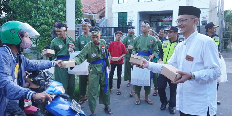 Ketua PC LDII Kecamatan Gunung Anyar, Giyato (kanan) bagikan takjil pada pengendara di kawasan jalan raya Ir Soekarno (MERR) Surabaya, Minggu (24/3). Dok: LINES.